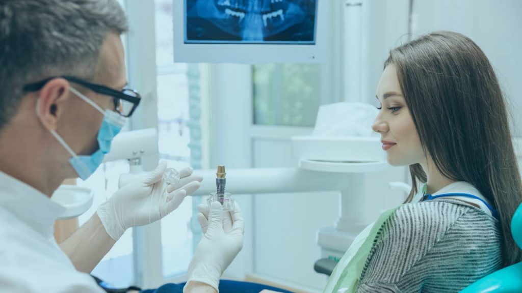 chirurgien dentiste montre un implant dentaire à sa patiente